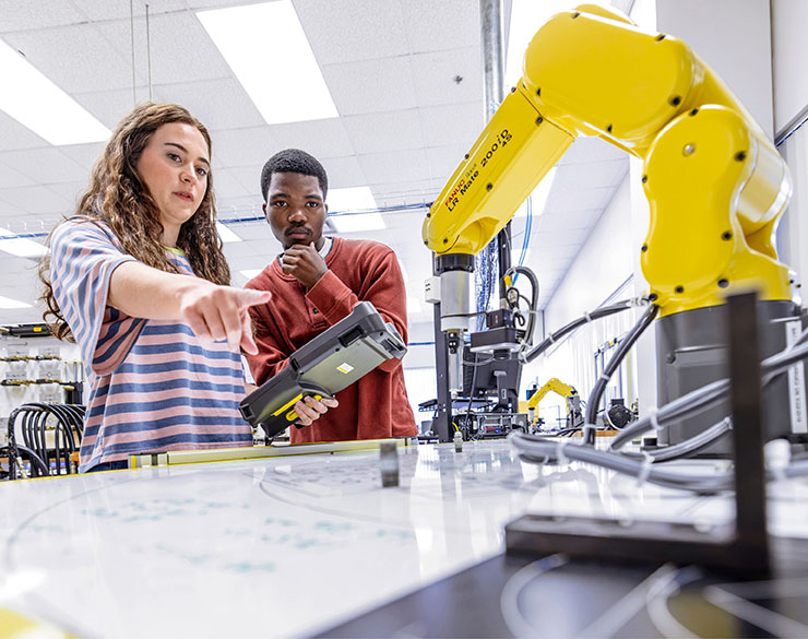 Two engineering students at Murray State operate robotic manufacturing equipment.