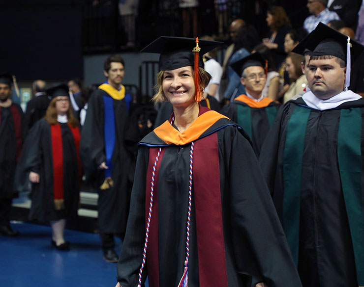 Woman smiles in her cap and gown at commencement