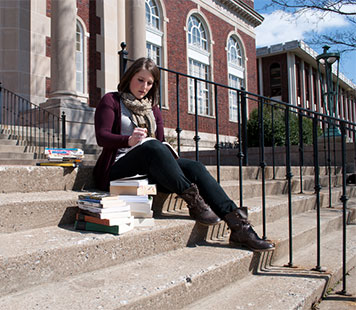 Student writes in notebook on steps. 