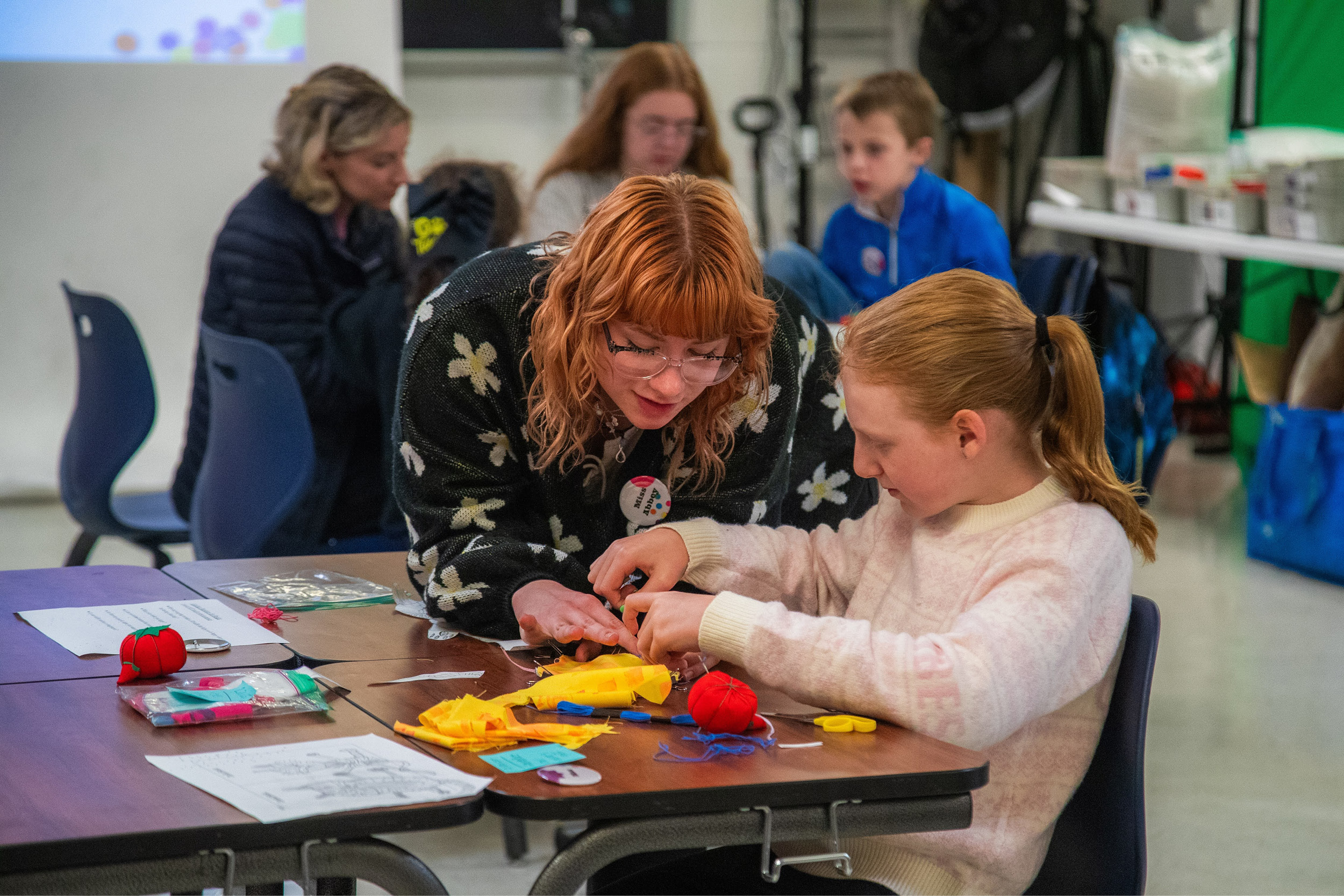 An art education student helps a girl assemble a felt tomato. 