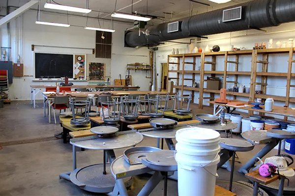 Overview of the ceramics facilities. A large room is filled with tables, with plenty of storage space along the wall, and pottery wheels in the back.