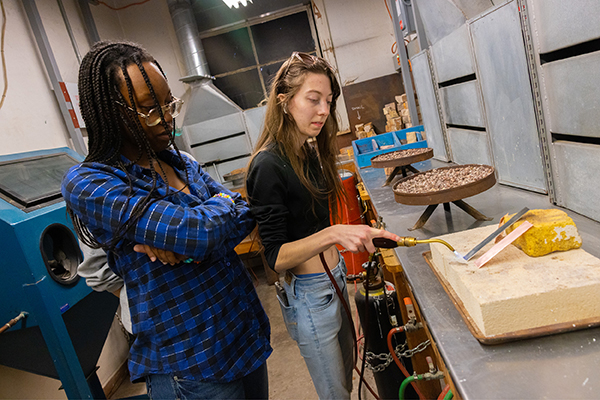 Two metalsmithing students use a heating tool to solder their project.