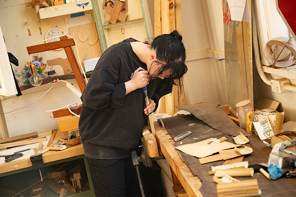 A woodworking student carves into a block of wood.