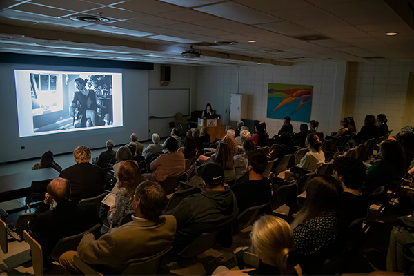 A large crowd of students gathers in the lecture hall as a visiting photographer discusses her work. 
