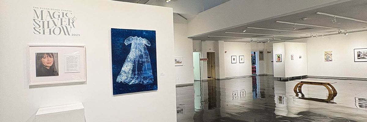 Entrance to the 2025 Magic Silver Show. At the front, the show title is printed on the wall above a photo and bio of the guest artist. A cyanotype of a dress is displayed beside it. Beyond that, the room opens to reveal more photos, with benches for sitting and reflecting on the artistry.
