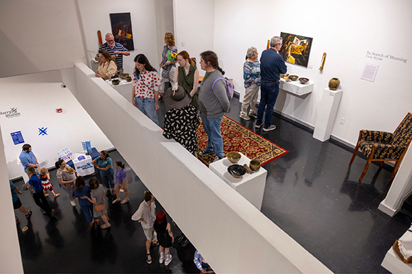 A small crowd of students, professors, and community members gathers together to look at the art on display in the Eagle Upper Gallery.