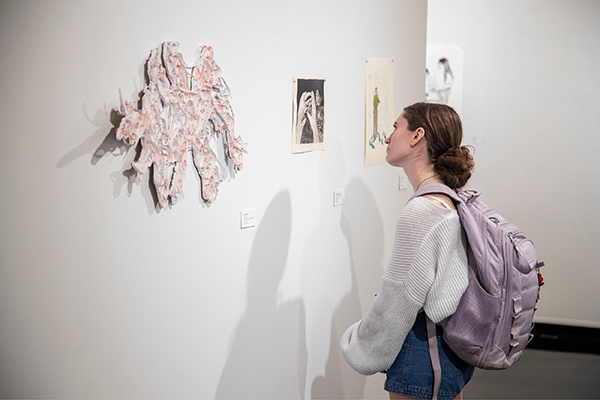 An art and design student contemplates a sculptural work displayed on the wall.