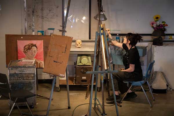 a student sits at an easel and paints a large canvas