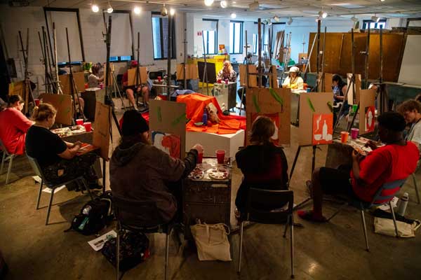 a circle of students paint individual canvases during class