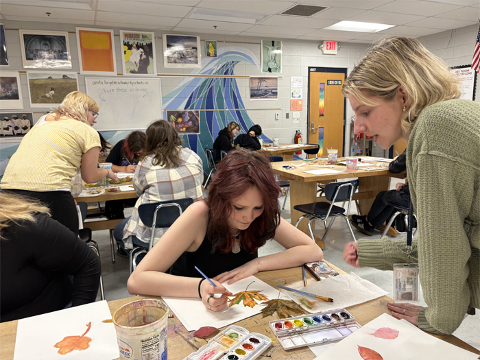 An art education student gives a high school student advice on her watercolor study of a leaf.