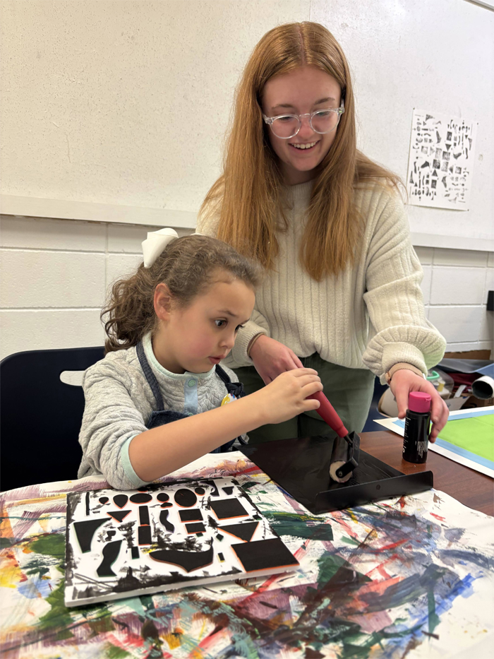 An art education student helps an elementary school student with a printmaking project.