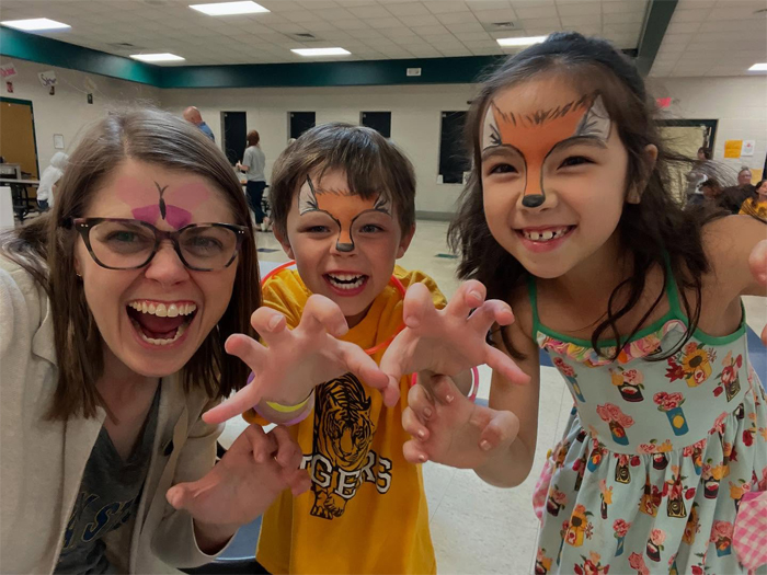 Dr. Rebecca Williams, with a butterfly painted on her face, poses with two elementary school children, their faces painted with fox ears and noses. 