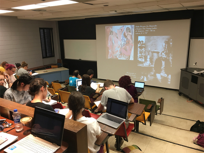 Art history students learn about Pablo Picasso, taking notes in their notebooks or on their laptops. 
