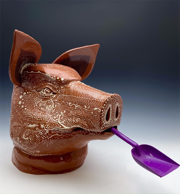 Decorative, ceramic pig’s head with a purple shovel protruding from its mouth, by Alum River Skipworth. 