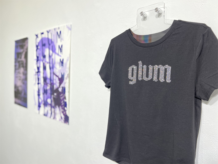 A black t-shirt on display, with the word “glum” bedazzled on it. 