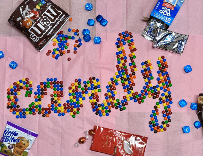 The word “candy” is spelled out using M&Ms. Assorted candies frame the text. 