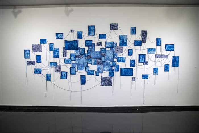 A collection of student-made cyanotypes is bound together and displayed like a large collage along the wall. 