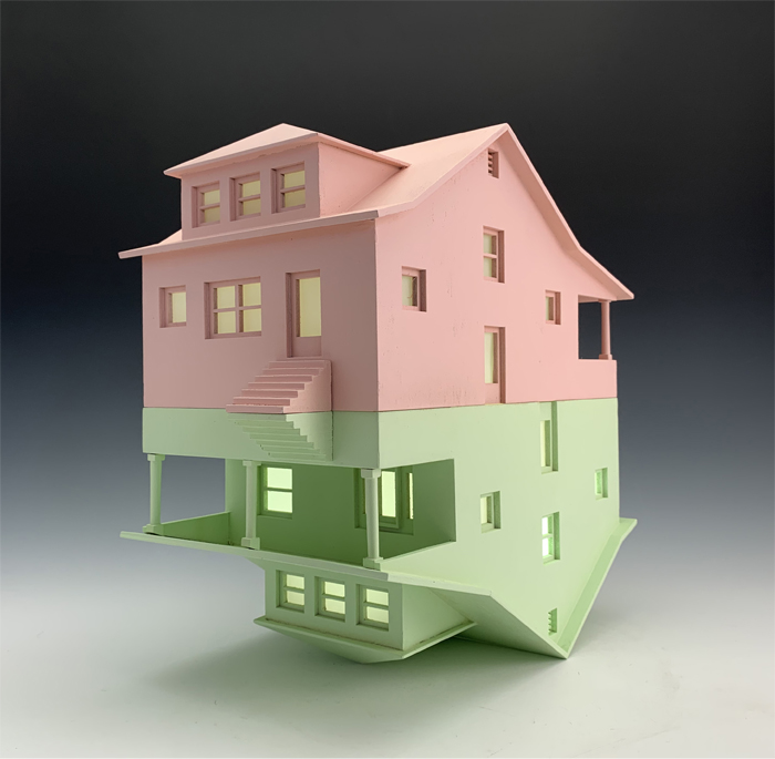 A wooden house sculpture that consists of a pink house perfectly mirrored on top of a green house. Artwork by student James Inmon. 