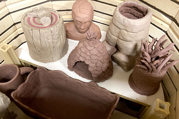 A kiln is filled with miscellaneous pottery, ranging from mugs and casserole dishes to busts and sculptures. 