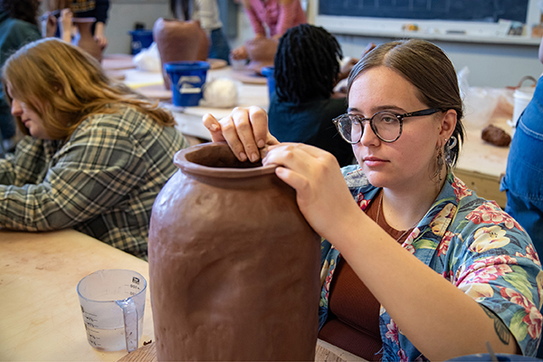 A ceramics student smoothes out the rim of a large vase. 