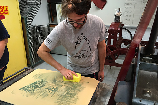 A printmaking student runs a sponge over his print to clean off the excess ink. 