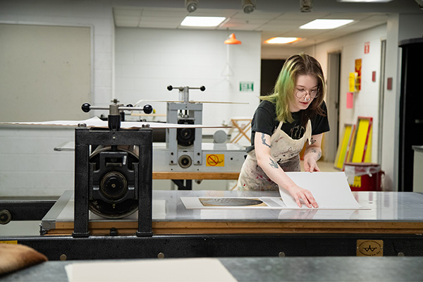A printmaking student operates a lithographic press. 