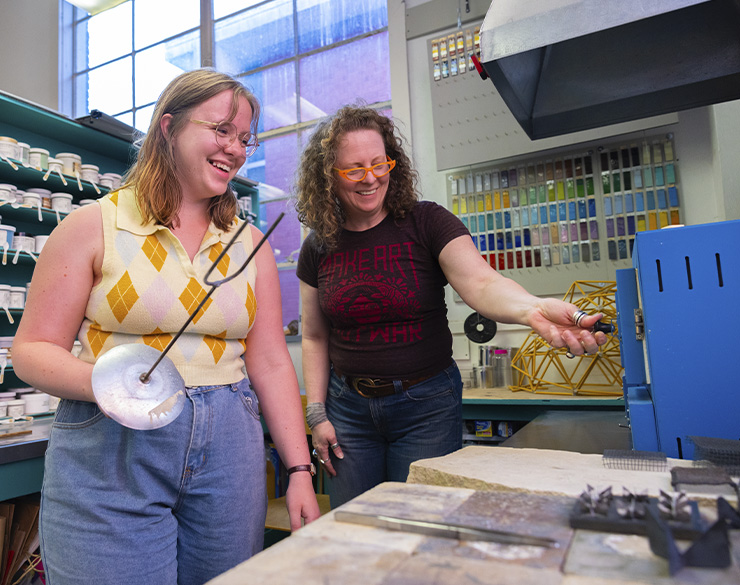 Two students studying metalsmithing smile as they work.
