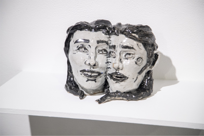 Ceramic sculpture of two smiling heads stitched together cheek-to-cheek.
