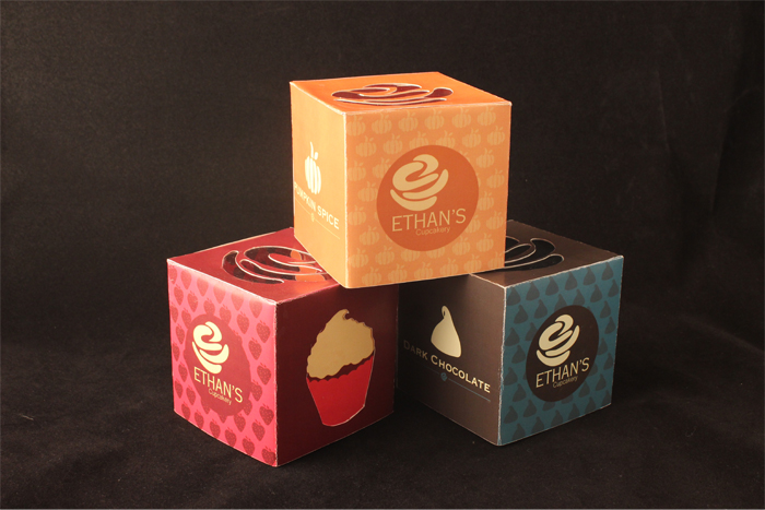A stack of three vibrant boxes advertising Ethan’s Cupcakery. 
