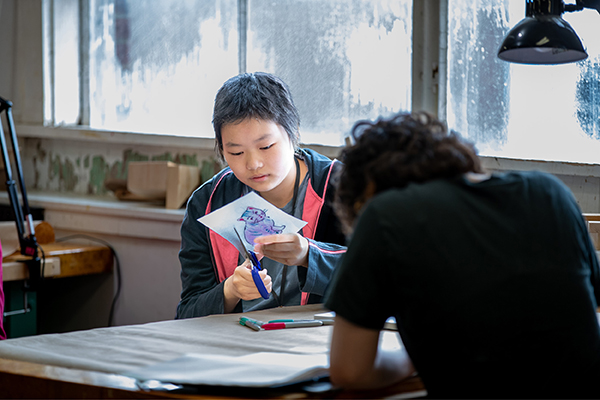 A SAW student cuts around an illustration of a cat made with Sharpies.