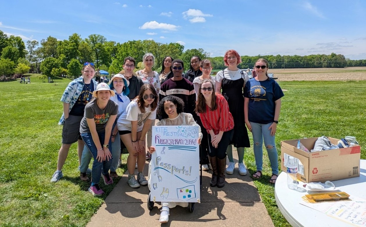 A group of AMG members in the Arboretum with a sign for the Kite Festival
