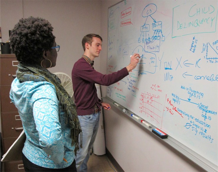 Student writing data on white board with research mentor