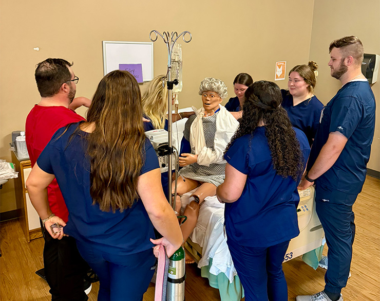 A group of OT students gather around a dummy to practice their skills