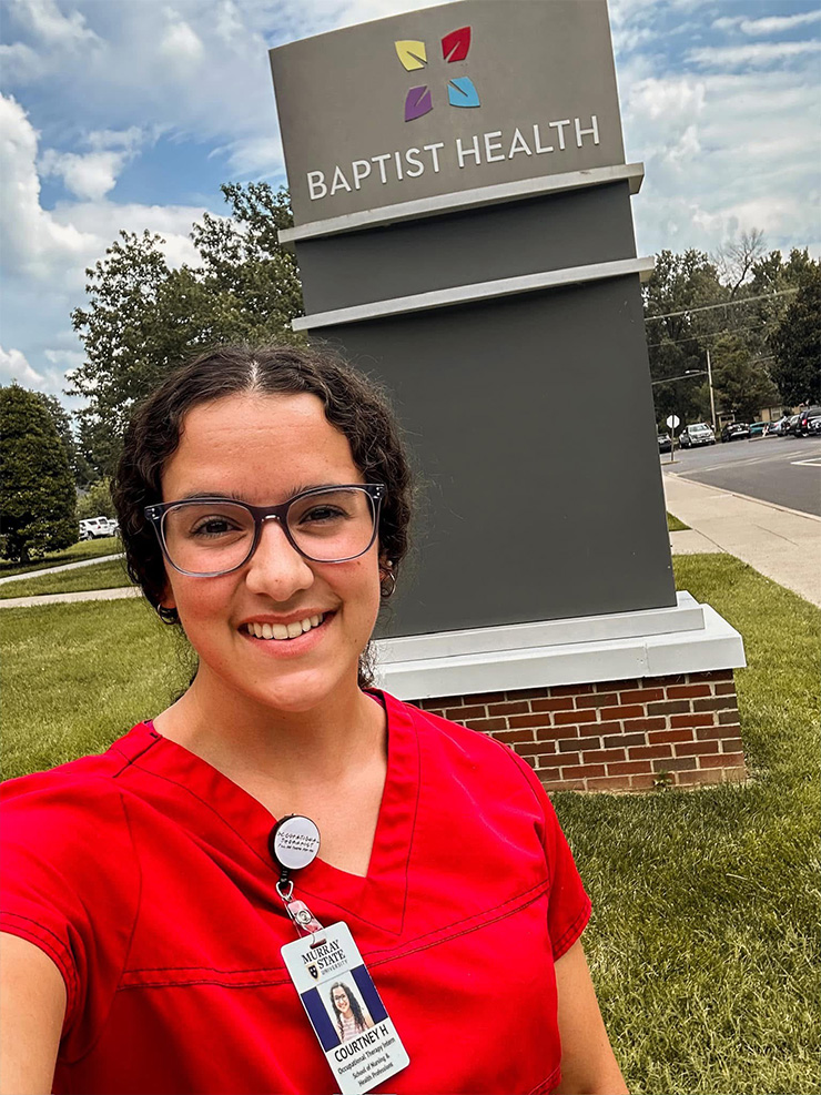 An OT student poses in front of the Baptist Health sign