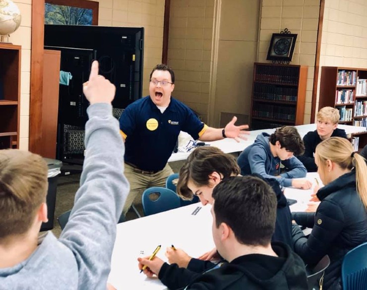 Campers sitting around a table, one camper has their finger raised in the air while the instructor looks excited