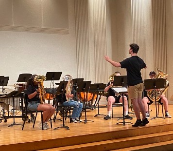Four RIMA campers practicing tuba with a conductor on stage