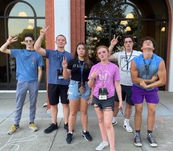 Six RIMA campers stand outside their residence hall making peace signs with their hands