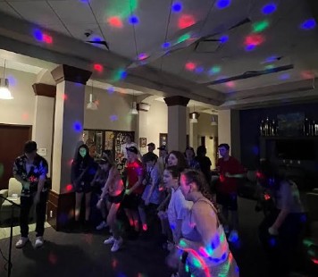 RIMA campers singing and dancing to karaoke in the lobby of their residence hall with colorful lights projected around the room