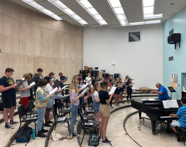 Chorus of campers practiving singing with conductor and piano player