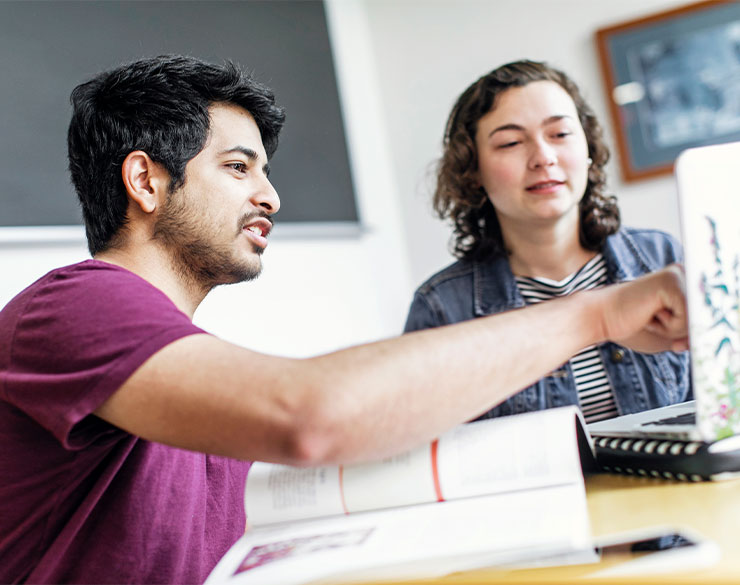 One student points to the laptop of another student. 