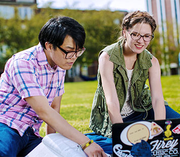 Two students look at a laptop on the Quad to learn more about college admissions