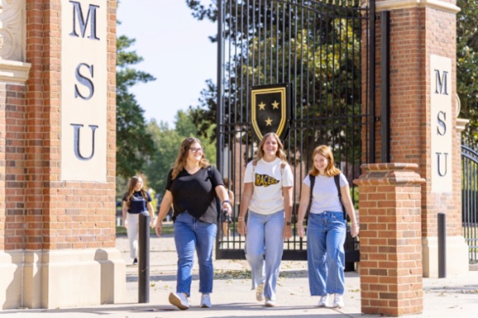 Three female students walking in front of brick gates that read MSU