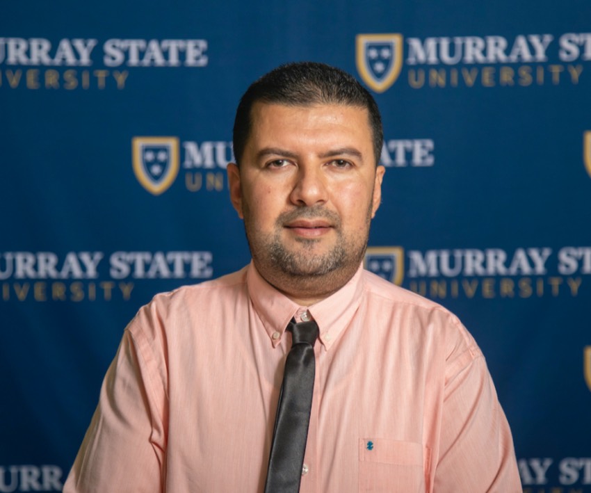 Dr. Hassan Mistareehi in a peach shirt and brown tie in front of a Murray State background.