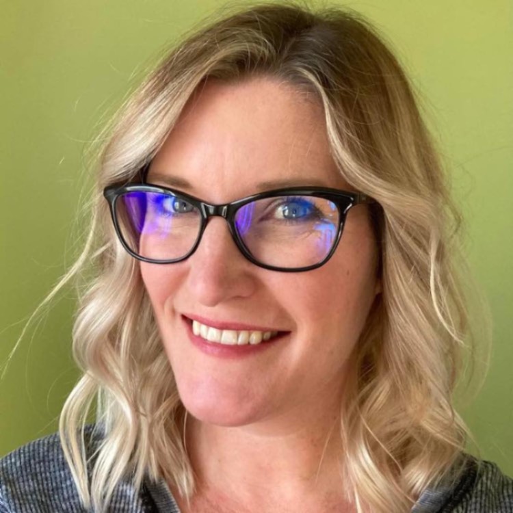 Dr. Laura Sullivan-Beckers in black glasses in front of a green background.