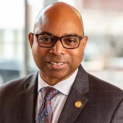Leon Owens in a suit, tie, white shirt, and glasses.