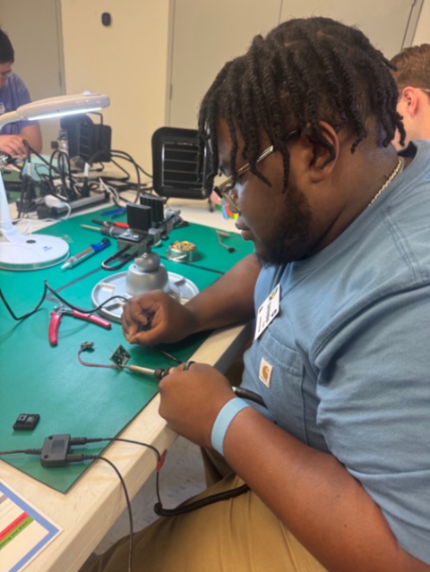 A student solders a tiny piece of electronic equipment.