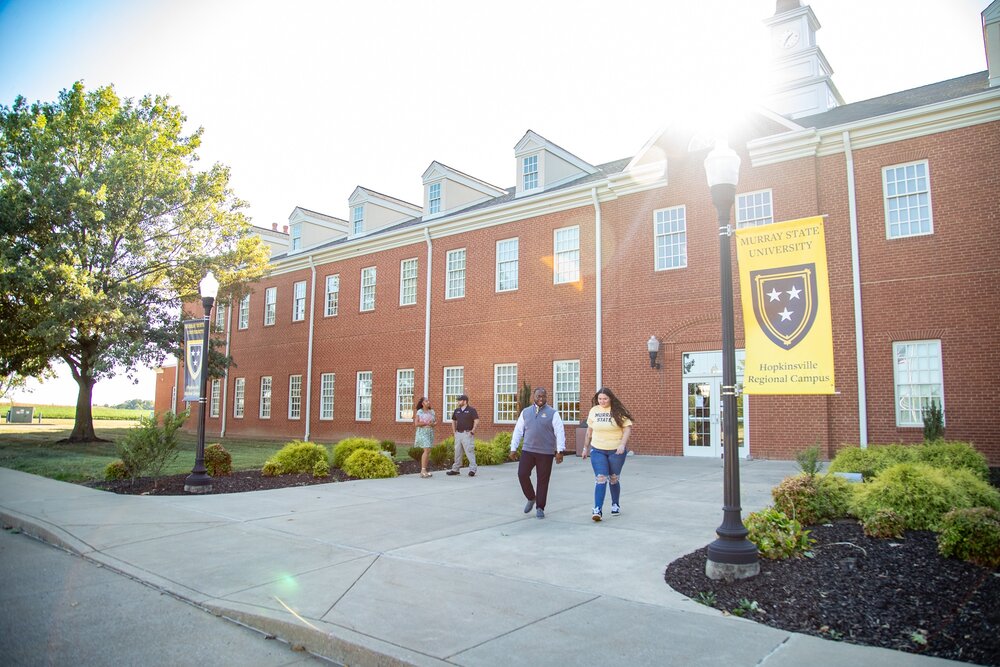 Students walking in front of a brick building on a sunny day.