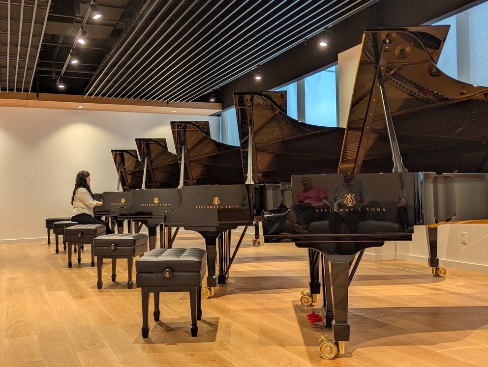 A woman plays a piano in the distance in a line of pianos