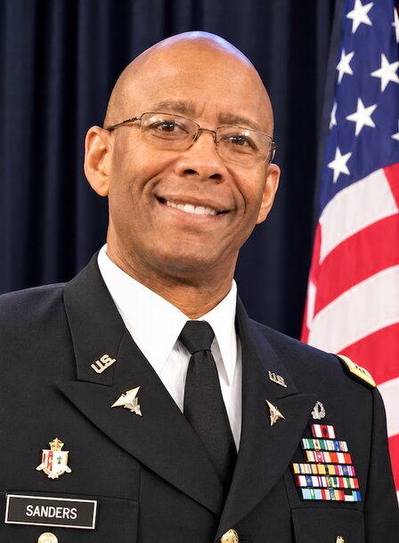 Ret. Col. Charlie Sanders in his uniform and glasses in front of an American flag.
