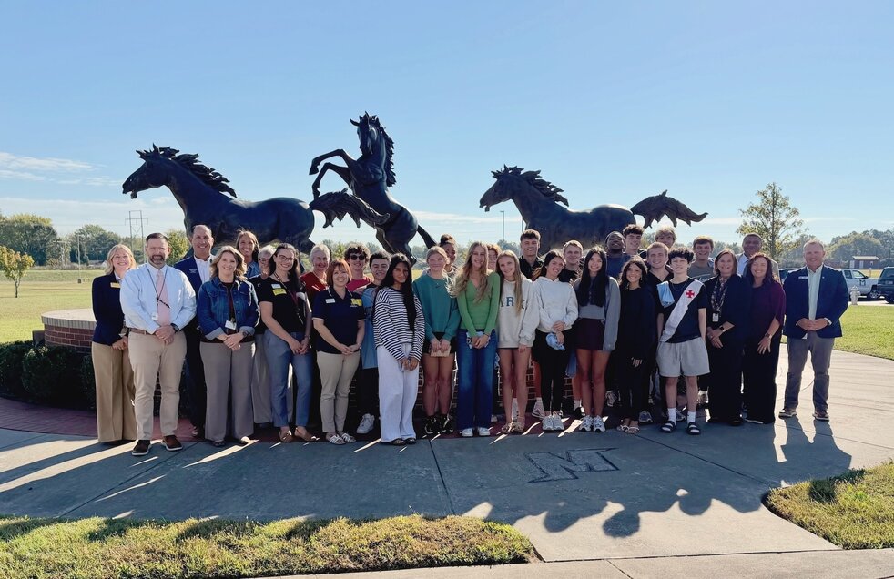 group of students and staff standing in front of three mustang statues